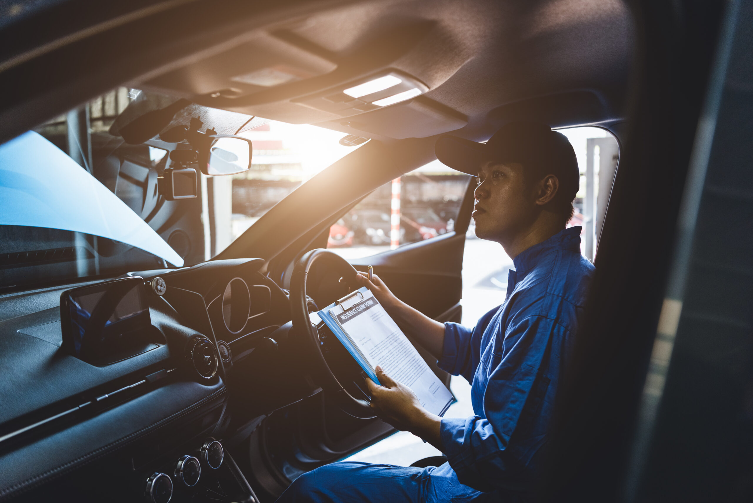 Mechanic holding clipboard and checking inside car to maintenance vehicle by customer claim order in auto repair shop garage. Repair service. People occupation and business job. Automobile technician