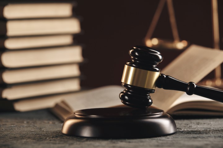 Law concept - Open law book with a wooden judges gavel on table in a courtroom or law enforcement office on blue background.