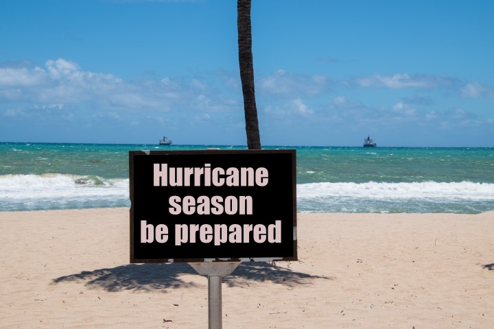 Warning sign on beach next to the trunk of a palm tree on a sunny day with a blue clear sky warning that it is hurricane season and that you should be prepared