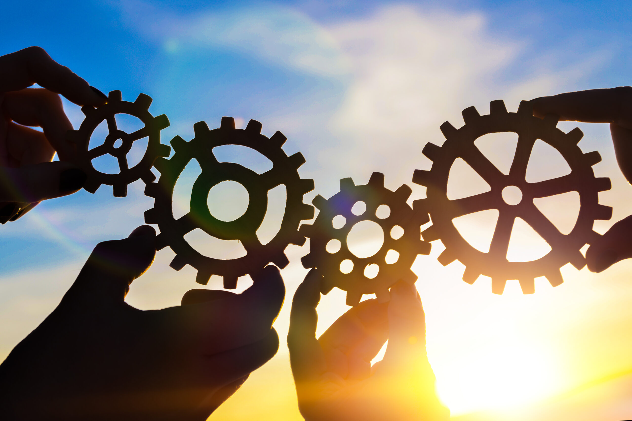 Four hands of businessmen collect gear from the gears of the details of puzzles. against the backdrop of dramatic sunlight. The concept of a business idea. Teamwork, strategy, cooperation, creativity